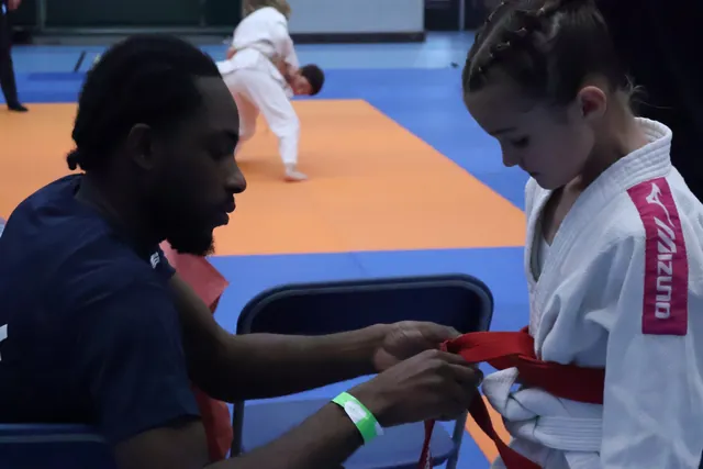 Begeleider helpt een jonge judoka met de wedstrijdriem
